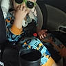 child, toddler, car_seat, car, sunglasses, green_sunglasses, pajamas, seated, portrait, indoor, vehicle, backseat, safety_harness, blond_hair, hand_gesture, fashion, playful, casual, photograph, travel