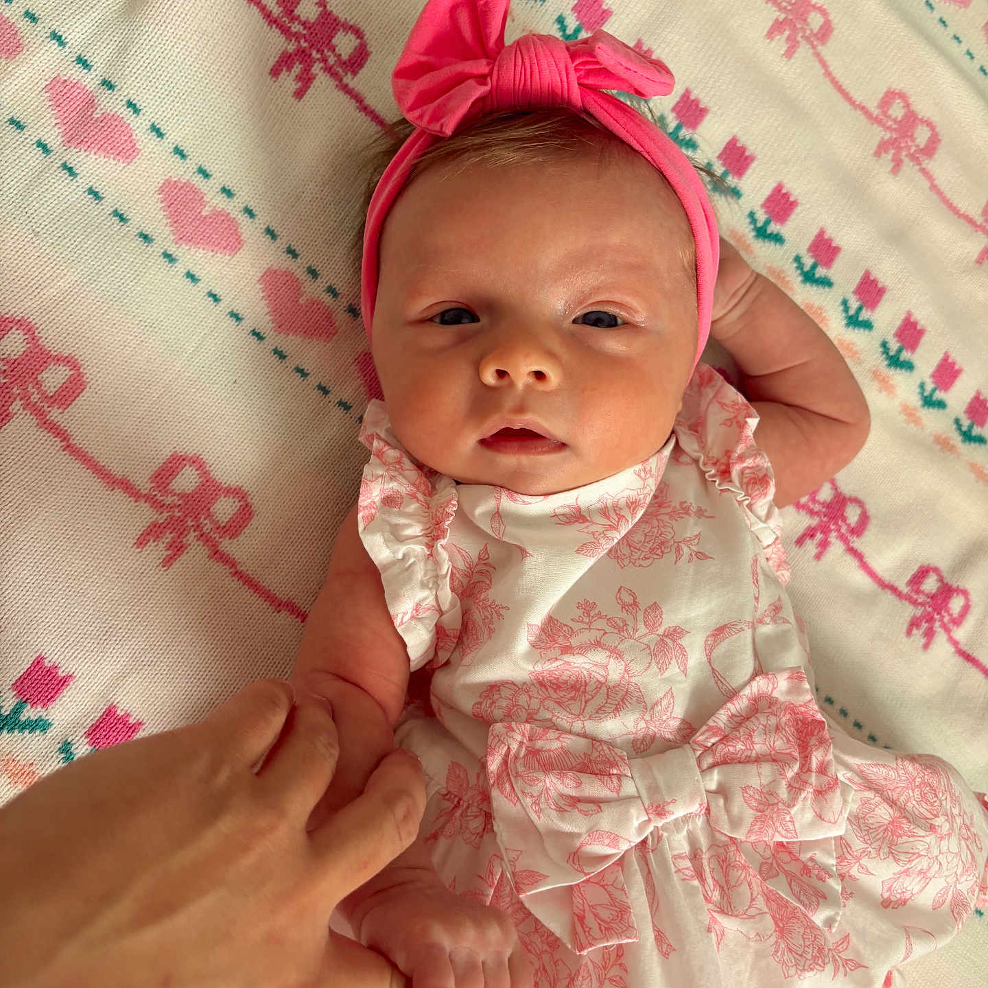 Gigi is registered to the contest to win money with this photo: baby, blanket, closeup, cute, dress, finger, floral_pattern, hand, headband, holding_hand, infant, lying_down, newborn, patterned_blanket, person, pink, skin, soft_lighting, tender, white