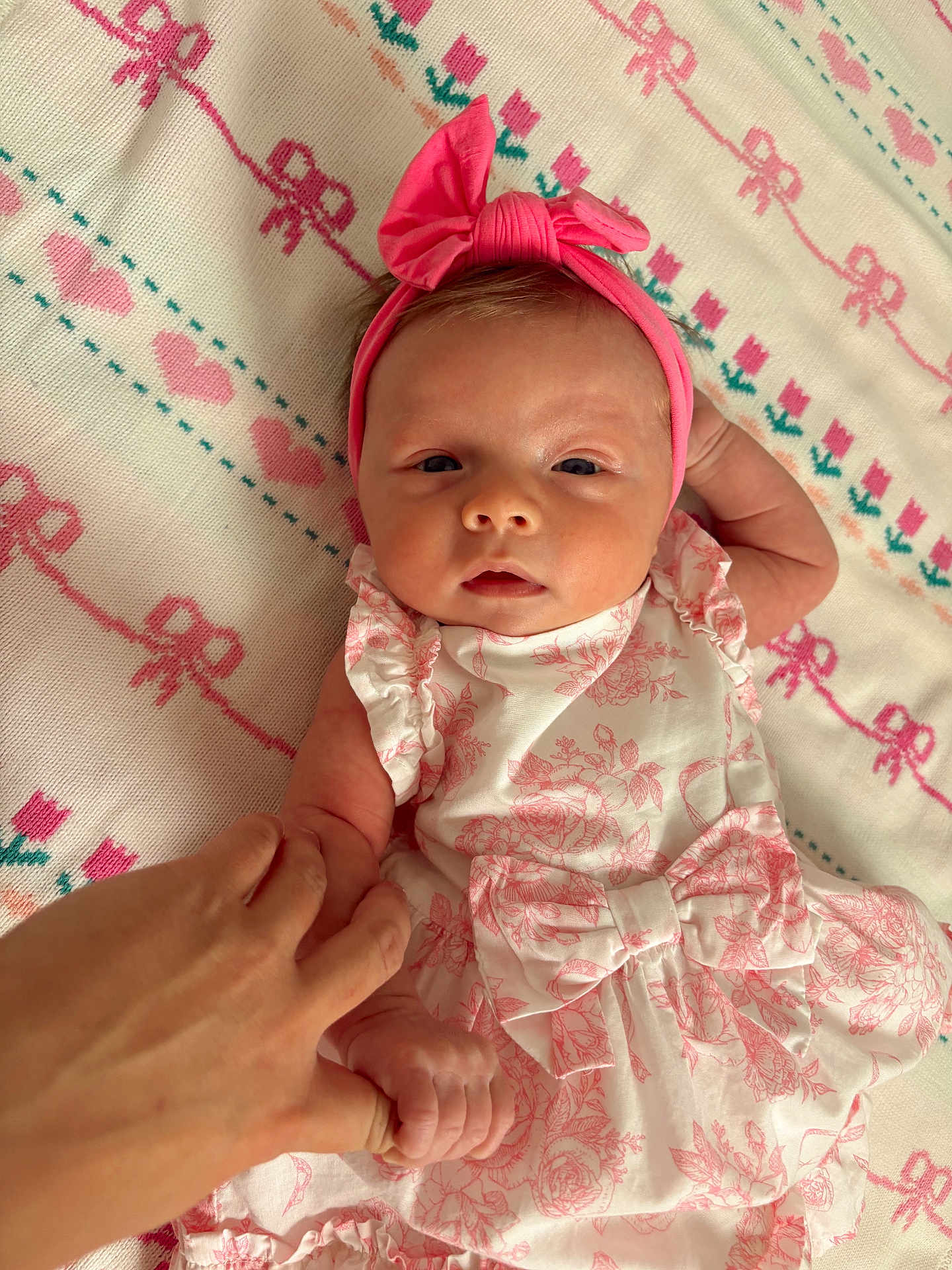 Gigi is registered to the contest to win money with this photo: baby, blanket, closeup, cute, dress, finger, floral_pattern, hand, headband, holding_hand, infant, lying_down, newborn, patterned_blanket, person, pink, skin, soft_lighting, tender, white