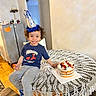 Adam is registered to the contest to win money with this photo: birthday, blueberries, cake, celebration, child, clothing, curly_hair, dessert, fruit, home, indoors, kitchen, lace, party_hat, portrait, seated, smiling, strawberries, table, tablecloth