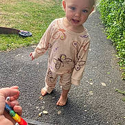 Kyra joined the competition — help win amazing prizes! toddler, child, barefoot, pajamas, butterfly_pattern, blonde_hair, blue_eyes, outdoor, paved_path, grass, bicycle, play_equipment, hand, colorful_object, curly_hair, casual_clothing, daylight, hedge, curious_expression, young_child