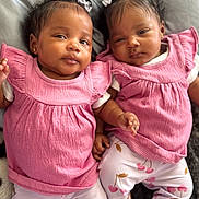 Trinity And Serenity is registered to the contest to win money with this photo: baby, twin, infant, pink_clothing, hair_bow, lying_down, cute, child, face, person, matching_outfits, white_socks, cherry_pattern, soft_surface, adorable, portrait, indoor, skin, head, small_hand