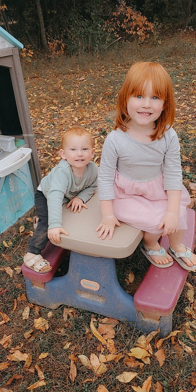 Maci is registered to the contest to win money with this photo: child, clothing, foot, fun, grass, happy, human_body, joy, lap, leg, leisure, people_in_nature, person, pink, play, recreation, shorts, sitting, smile, t_shirt