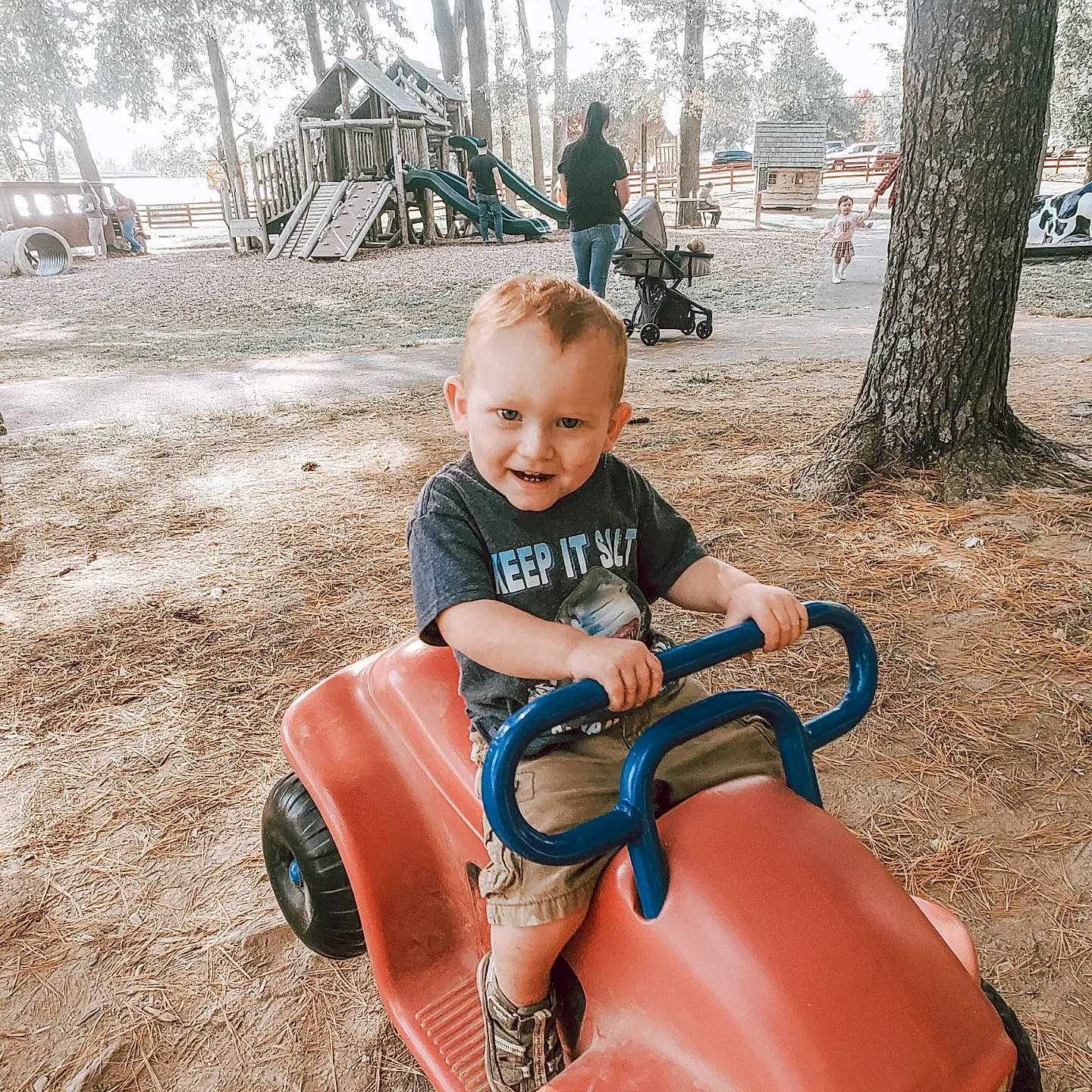 Jaxson is registered to the contest to win money with this photo: automotive_tire, baby, child, city, fun, grass, happy, joy, leisure, motor_vehicle, person, recreation, riding_toy, shorts, sitting, smile, tire, toddler, travel, tree
