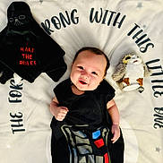 Elijah is registered to the contest to win money with this photo: baby, infant, child, smiling, lying_down, portrait, black_outfit, costume, blanket, star_pattern, stuffed_toy, penguin, darth_vader, toy, nursery, indoor, happy, face, textile, photography
