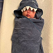 Elijah joined the competition — help win amazing prizes! baby, towel, shark_costume, wrapped, cute, infant, face, child, portrait, blanket, soft_texture, indoor, adorable, head, expression, pout, young_child, cozy, person, resting
