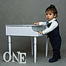 Dominick is registered to the contest to win money with this photo: bow_tie, child, dark_pants, dress_shoes, formal_clothing, gray_background, indoor, keyboard, lettering, looking_at_camera, musical_instrument, one, piano, portrait, standing, studio, suit, toddler, vest, white_shirt