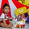 admit_one, animal_characters, balloons, birthday, bow_tie, cake, celebration, child, circus_theme, colorful, decorations, indoor, party, popcorn, portrait, red_clothing, sitting, suspenders, toddler, wide_eyes