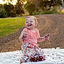 baby, child, outdoor, sunset, smiling, cake, messy, face, hands, blanket, dirt_path, grass, pink_top, floral_pants, happy, sitting, food, celebration, nature, portrait