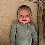 baby, infant, smiling, green_onesie, carpet, cushion, blanket, indoors, child, person, cute, lying_down, happy, face, head, small_person, cozy, home, comfort, soft_texture