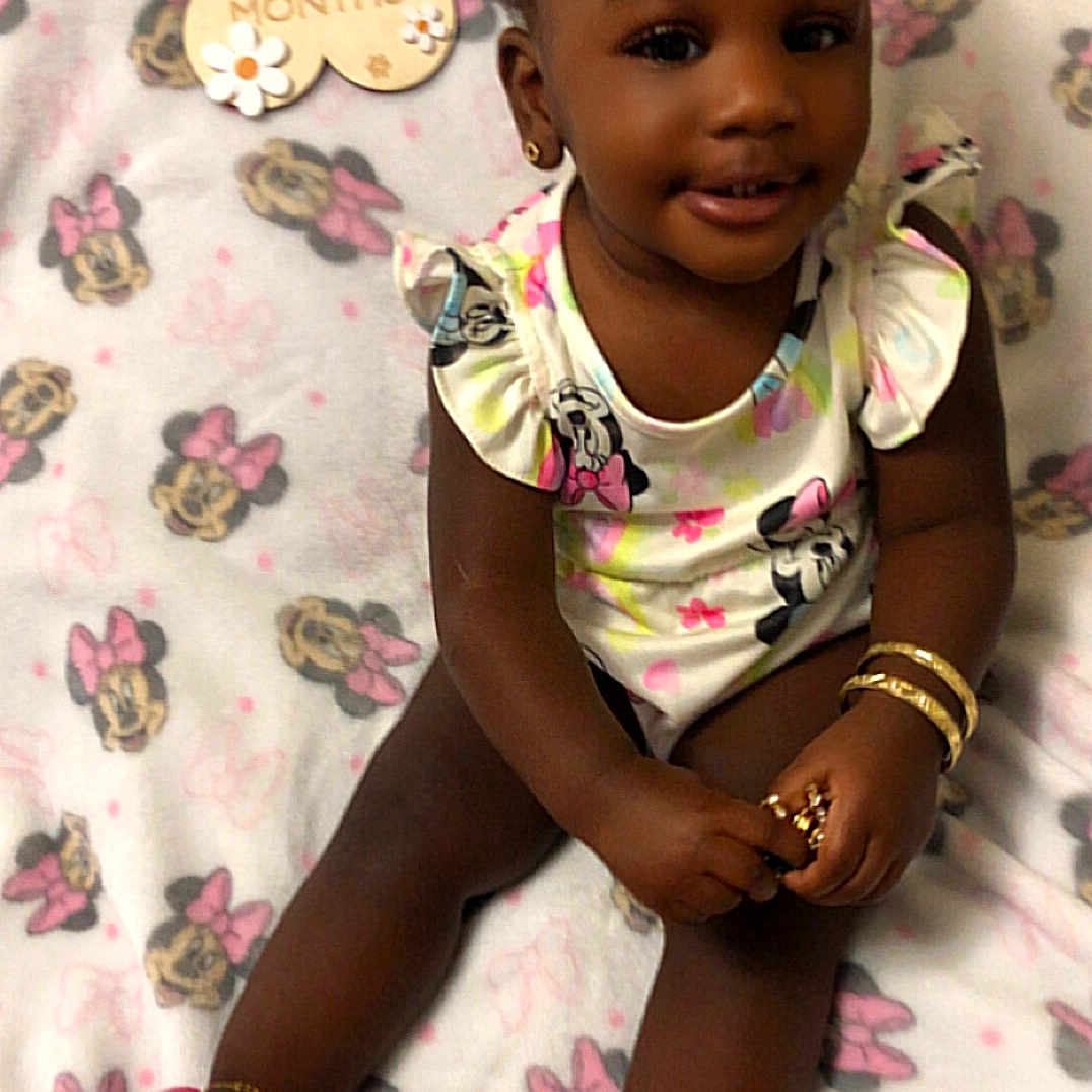 Ariis is registered to the contest to win money with this photo: baby, child, infant, girl, smile, sitting, blanket, minnie_mouse, clothing, footwear, jewelry, milestone, pink, cute, happy, indoors, portrait, accessories, toy, celebration