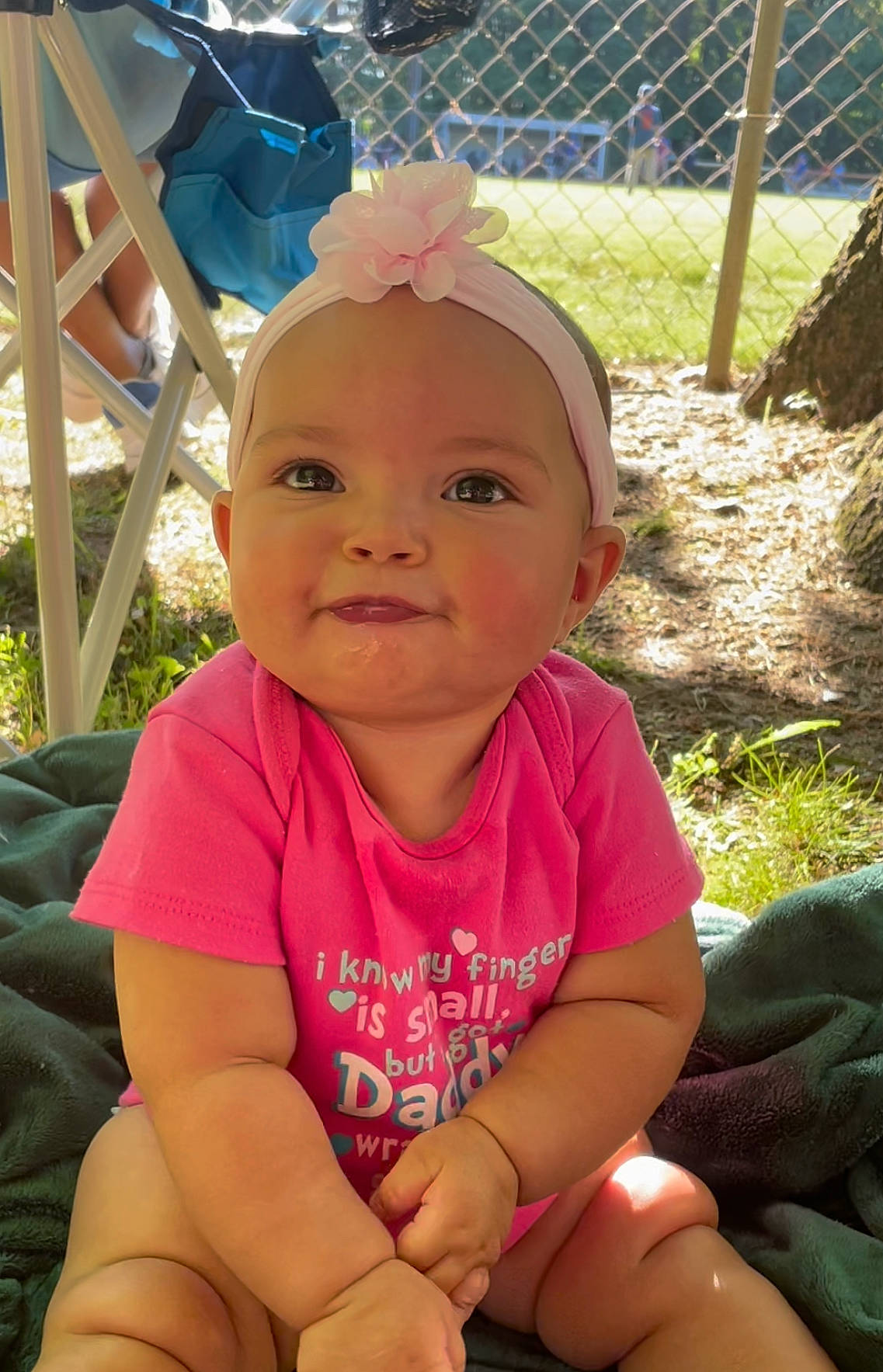 Octavia is registered to the contest to win money with this photo: baby, baby_toddler_clothing, blue, cap, child, facial_expression, fashion_accessory, fun, grass, happy, head, headwear, leisure, magenta, people_in_nature, person, pink, recreation, sitting, skin