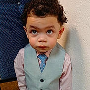 Benjamin is registered to the contest to win money with this photo: child, boy, curly_hair, vest, tie, shirt, indoor, portrait, looking_up, face, expression, formal_clothing, young, person, wall, chair, pattern, texture, cute, fashion