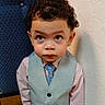 Benjamin is registered to the contest to win money with this photo: boy, chair, child, curly_hair, cute, expression, face, fashion, formal_clothing, indoor, looking_up, pattern, person, portrait, shirt, texture, tie, vest, wall, young