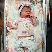 Emarelys is registered to the contest to win money with this photo: newborn, baby, infant, sleeping, bassinet, blanket, pink_clothing, headband, bow, plush_toy, rainbow_pattern, hospital, soft_toys, footwear, cute, peaceful, indoors, person, child, cozy