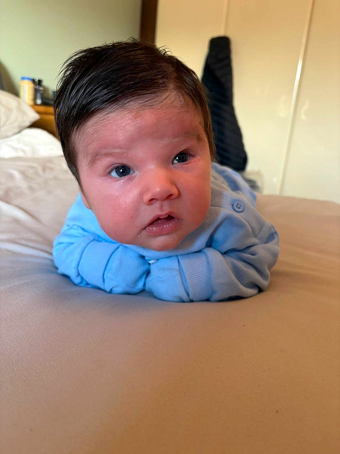 Alexander is registered to the contest to win money with this photo: baby, infant, blue_clothing, bed, blanket, face, eyes, expression, skin, hair, indoor, person, child, young, portrait, bedroom, sleeve, cute, lying_down