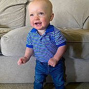 Preston is registered to the contest to win money with this photo: toddler, child, smiling, standing, indoor, couch, clothing, jeans, polo_shirt, blue, striped, carpet, footwear, happy, person, young_child, cute, face, short_hair, home