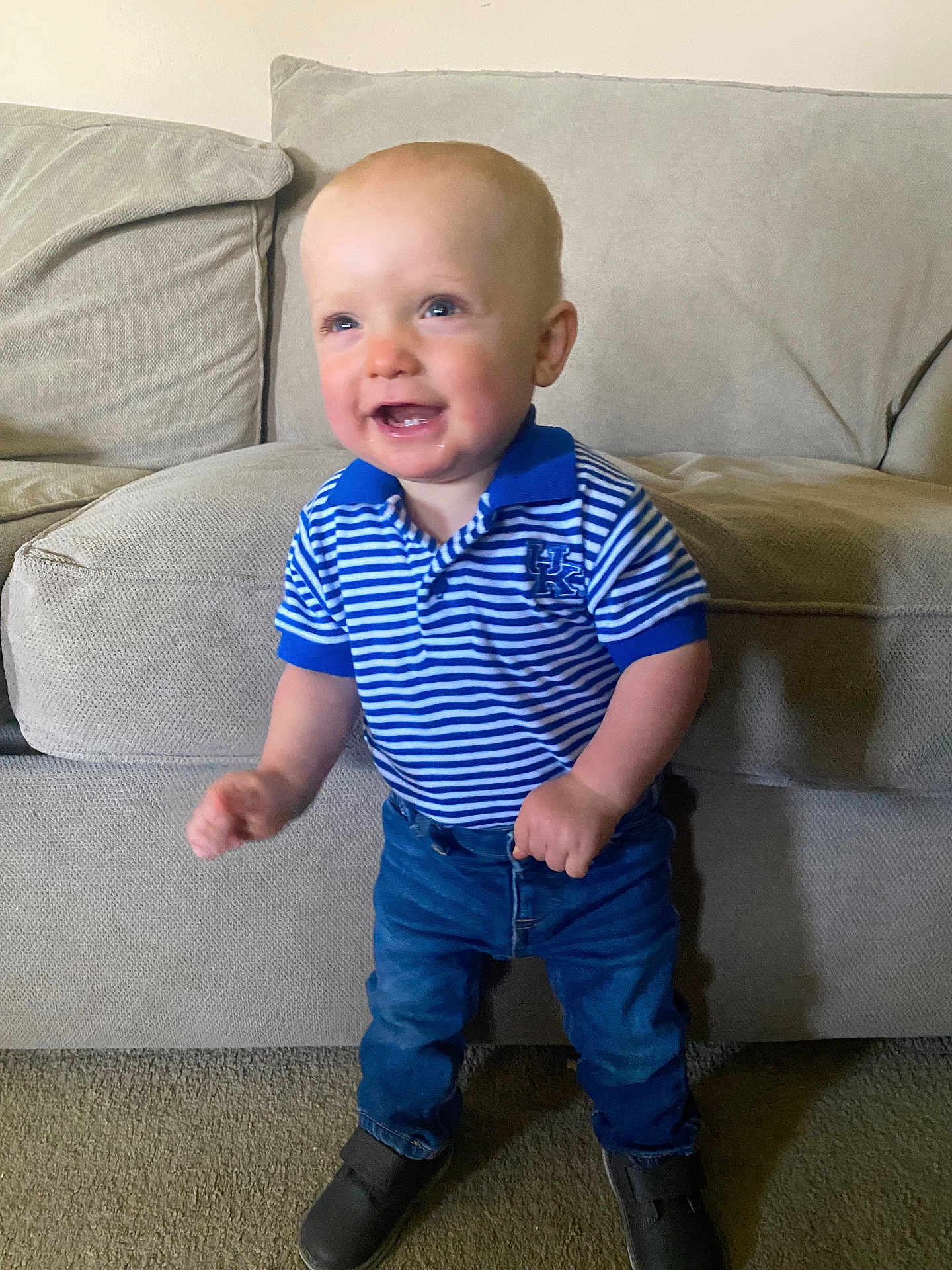 Preston is registered to the contest to win money with this photo: toddler, child, smiling, standing, indoor, couch, clothing, jeans, polo_shirt, blue, striped, carpet, footwear, happy, person, young_child, cute, face, short_hair, home