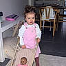 chair, child, cozy, curly_hair, dining_table, doll, floor, furniture, home, indoor, kitchen, modern, person, pink_overalls, playtime, rug, stroller, toddler, toy, white_shirt