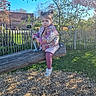 child, daytime, expression, face, fence, grass, jacket, nature, outdoor, park, person, pink_tights, play, playground, sneakers, spring, sunlight, toddler, tree, wooden_seesaw