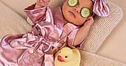 Dakota is registered to the contest to win money with this photo: baby, infant, child, sleeping, portrait, cucumber, rubber_duck, pink_outfit, satin, bonnet, bow, couch, blanket, indoor, spa, humorous, relaxed, face, toy, photography