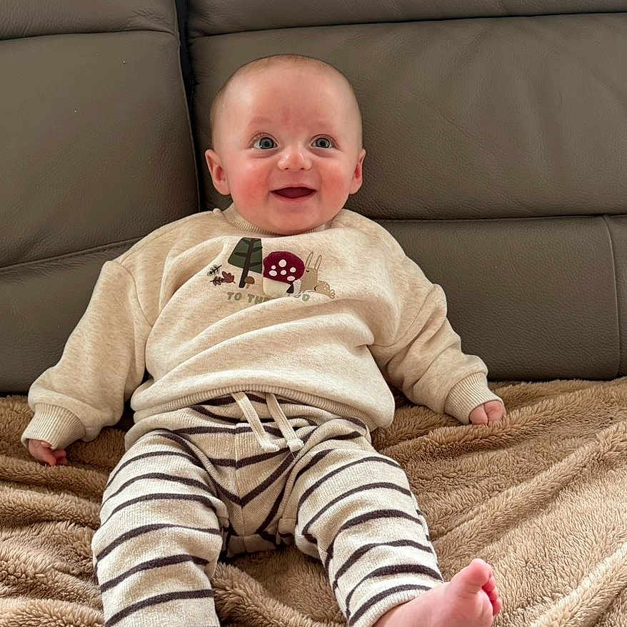 Marco participe au concours pour gagner de l'argent avec cette photo : baby, child, smiling, sitting, blanket, couch, sweater, striped_pants, indoor, cozy, happy, face, feet, toes, person, furniture, soft_texture, cute, young, portrait