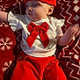 baby, infant, child, red_hat, red_shorts, white_top, red_bow, blanket, snowflake_pattern, zigzag_pattern, holiday_theme, cute, portrait, laying_down, indoor, clothing, person, face, soft_lighting, festive