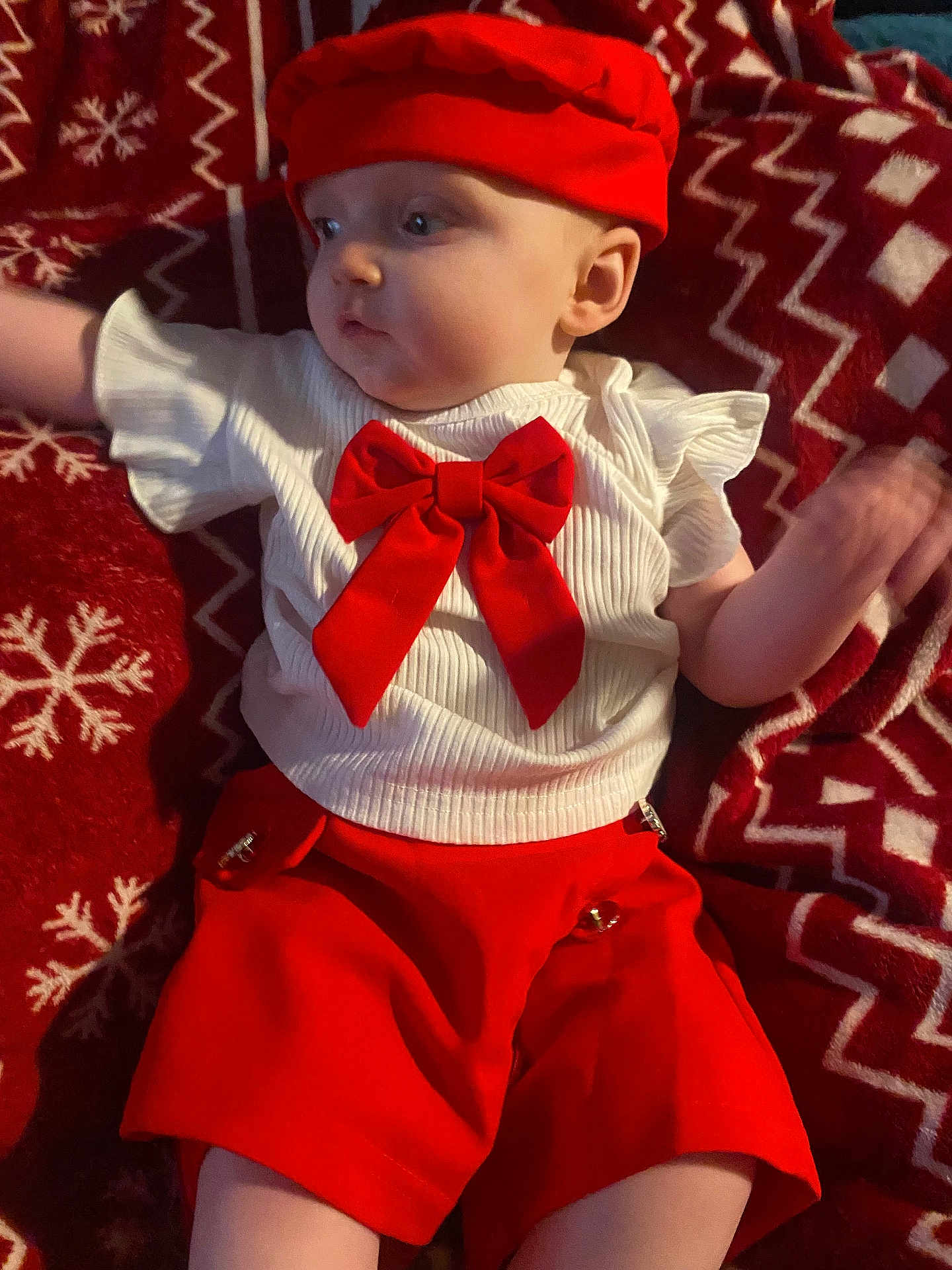 Talia Satin joined the competition — help win amazing prizes! baby, infant, child, red_hat, red_shorts, white_top, red_bow, blanket, snowflake_pattern, zigzag_pattern, holiday_theme, cute, portrait, laying_down, indoor, clothing, person, face, soft_lighting, festive