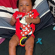 Aaliyah is registered to the contest to win money with this photo: baby, infant, onesie, minnie_mouse, red_clothing, socks, pacifier, pillow, striped_pillow, black_hair, curly_hair, indoor, couch, child, person, cute, smiling, relaxed, lying_down, portrait
