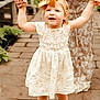 child, toddler, holding_hands, orange_bow, floral_dress, adult, walking, outdoor, cobblestone, plants, sandals, smiling, cute, person, family, summer, happy, fashion, footwear, nature