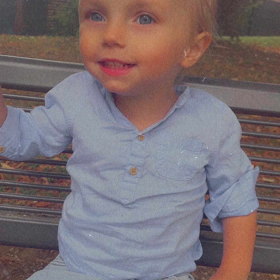 Cayden a rejoint le concours — aidez-le/la à gagner de superbes lots ! bench, blue_eyes, casual_clothing, child, cute, daylight, happy, light_blue, metal_bench, nature, outdoor, pants, park, person, portrait, shirt, sitting, smiling, toddler, young_child