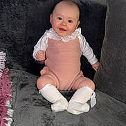 Scarlett is registered to the contest to win money with this photo: baby, child, infant, smiling, sitting, couch, sofa, white_socks, pink_romper, knitted_clothing, indoor, home, cozy, plush, happy, portrait, person, face, cute, comfortable