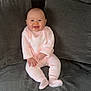 baby, smiling, pink_outfit, couch, grey_cushions, indoor, child, happy, seated, plush, cozy, portrait, cute, infant, comfort, soft_fabric, sitting, one_person, casual_clothing, relaxed