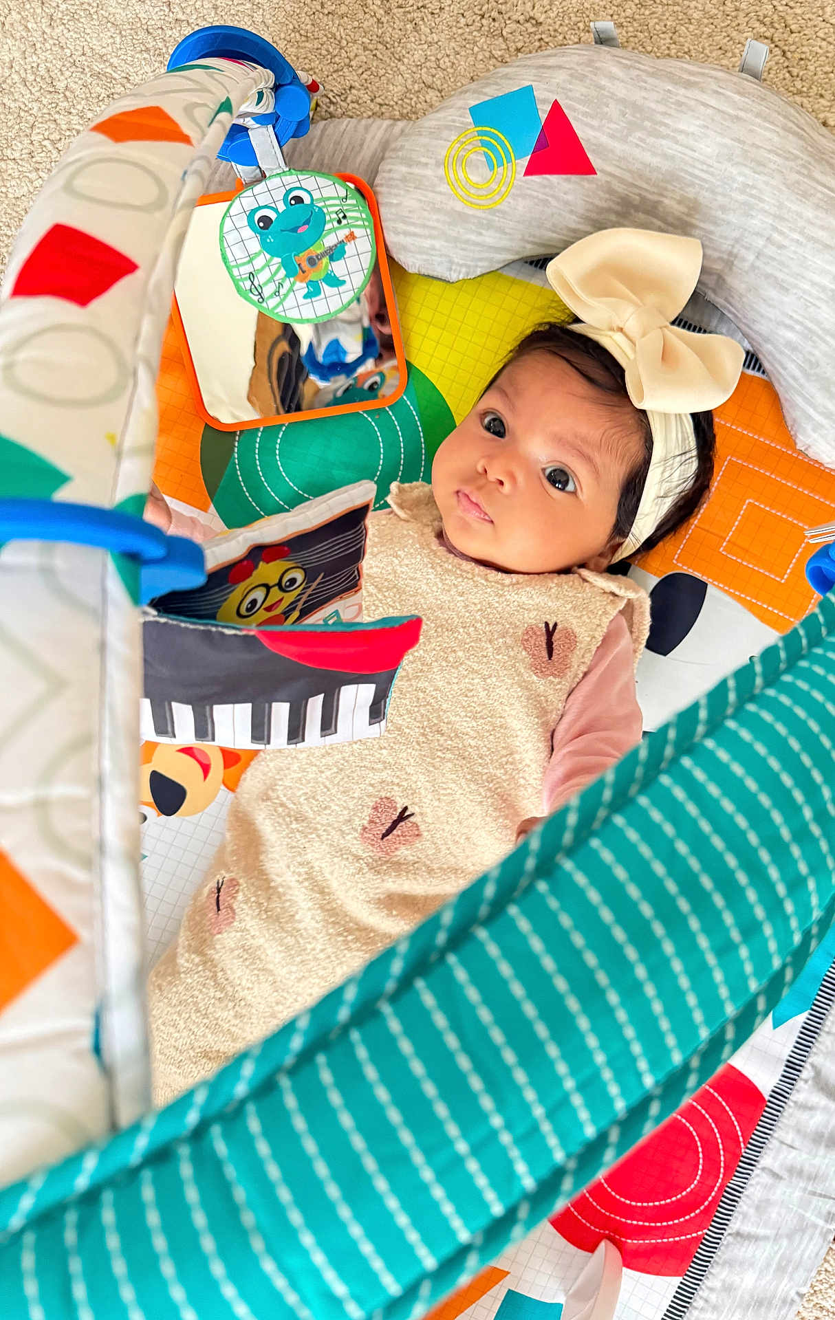 Joudia a rejoint le concours — aidez-le/la à gagner de superbes lots ! baby, infant, headband, bow, play_mat, toy, mirror, colorful, carpet, floor, child, cute, expression, looking_up, patterned_clothing, soft_toys, indoor, young, face, eyes