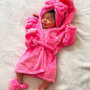 Joudia a rejoint le concours — aidez-le/la à gagner de superbes lots ! newborn, baby, pink_robe, sleeping, soft_texture, blanket, footwear, bow, cozy, infant, cute, child, clothing, indoor, portrait, peaceful, resting, warm, adorable, toddler