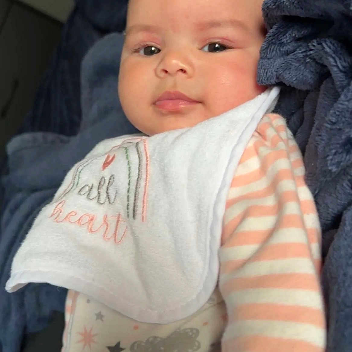 Iyla joined the competition — help win amazing prizes! baby, bed, bib, blanket, child, close_up, cozy, cuddly, eyes, face, indoors, infant, onesie, pajamas, photography, portrait, sitting, smiling, striped_clothing, textile