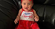 Iyla is registered to the contest to win money with this photo: baby, barefoot, blue_eyes, child, close_up, festive, fireworks_pattern, headband, indoors, infant, leather_couch, leather_furniture, patriotic, photography, portrait, red_bow, red_dress, sitting, smiling, surprised_expression