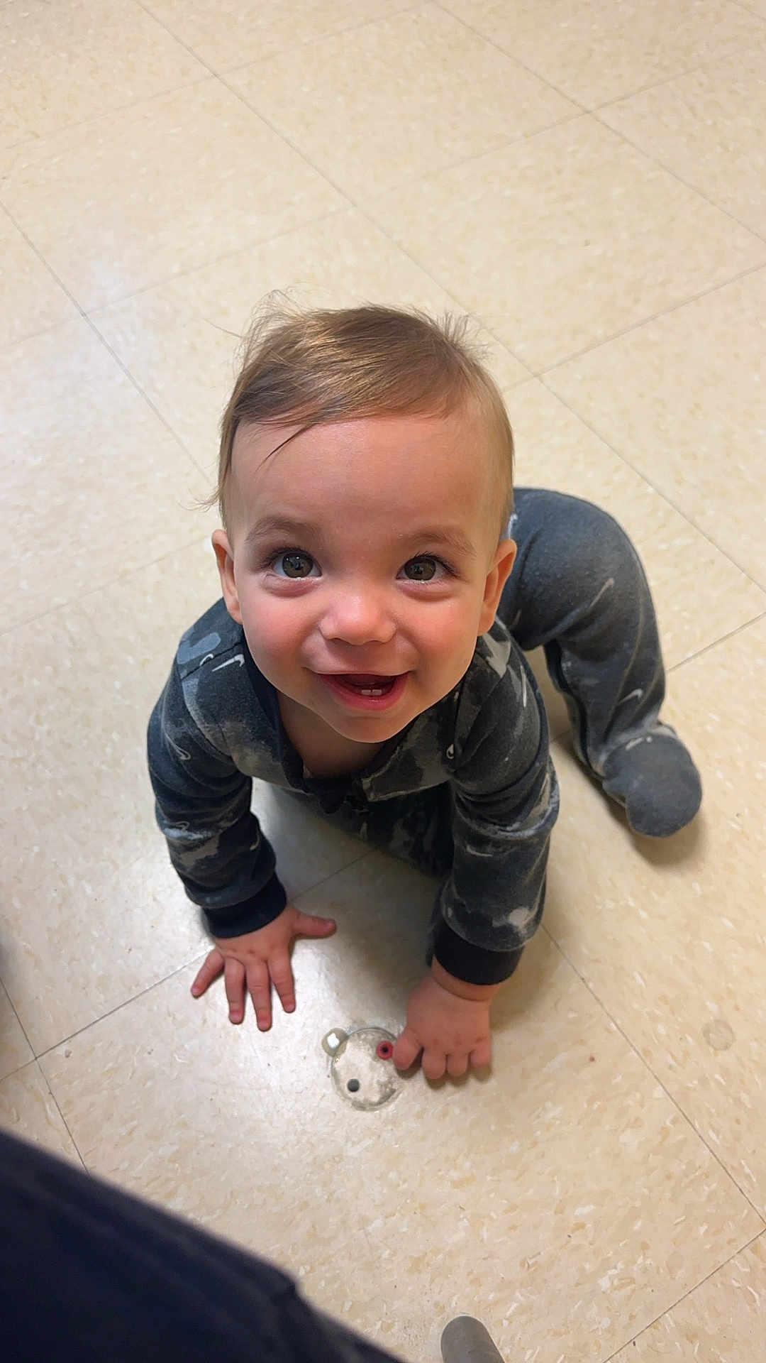 Xander is registered to the contest to win money with this photo: toddler, child, pajamas, floor, tile, crawling, smiling, happy, indoor, baby, person, cute, playing, small_object, holding, head, hands, eyes, mouth, clothing