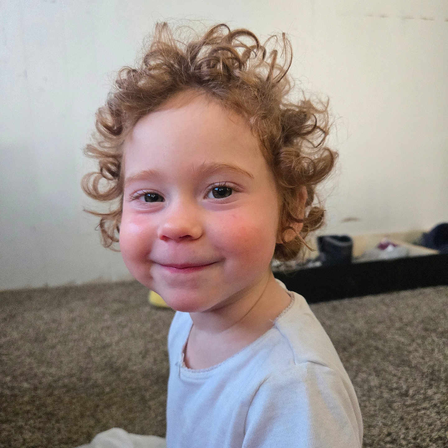 Sabrina joined the competition — help win amazing prizes! child, toddler, curly_hair, smile, indoor, carpet, face, person, white_shirt, rosy_cheeks, young_child, happy, cute, portrait, sitting, young_person, expression, head_and_shoulders, casual_clothing, home