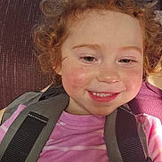 Sabrina is registered to the contest to win money with this photo: child, toddler, curly_hair, smiling, pink_shirt, striped_shirt, harness, happy, face, rosy_cheeks, person, portrait, seated, indoors, closeup, cute, young_child, skin, hair, casual_clothing