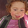 child, toddler, curly_hair, smiling, pink_shirt, striped_shirt, harness, happy, face, rosy_cheeks, person, portrait, seated, indoors, closeup, cute, young_child, skin, hair, casual_clothing