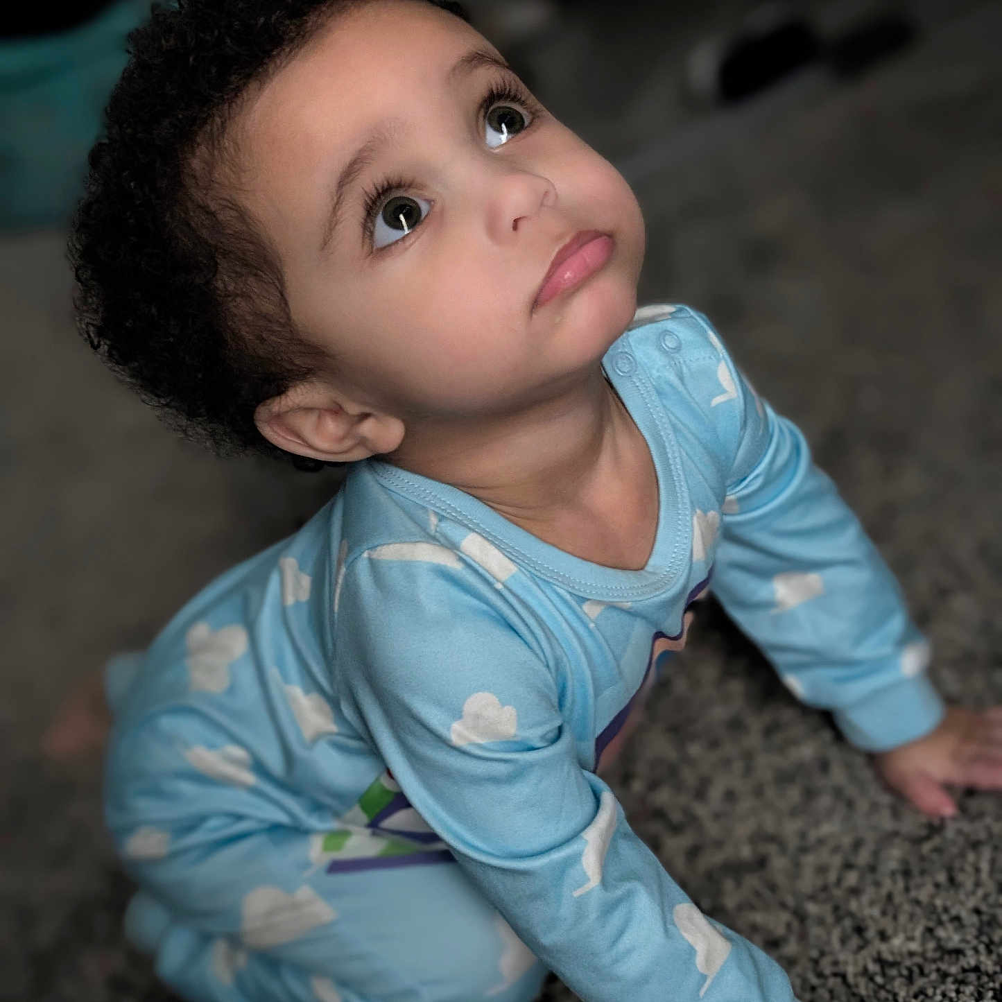 Everett is registered to the contest to win money with this photo: baby, blue_clothing, carpet, child, clothing, curly_hair, cute, expression, eyes, face, floor, hands, indoor, long_sleeve, looking_up, pajamas, person, skin, toddler, young_child