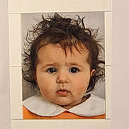 Yéva a rejoint le concours — aidez-le/la à gagner de superbes lots ! baby, portrait, child, face, hair, curly_hair, expression, clothing, white_collar, orange_outfit, studio_lighting, photo_print, date_stamp, indoor, headshot, young_child, innocent_look, closeup, person, photograph