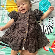 Annie joined the competition — help win amazing prizes! baby, child, smiling, curly_hair, dress, play_mat, colorful, animal_print, buttoned_dress, lying_down, happy, infant, cute, indoors, person, skin, arms, legs, soft_lighting, portrait
