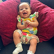 Annie joined the competition — help win amazing prizes! baby, smiling, child, colorful_clothing, white_socks, red_pillows, couch, indoor, happy, cute, infant, sitting, portrait, young_child, playful, cozy, fabric, home, person, expression