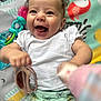 Annie joined the competition — help win amazing prizes! baby, smiling, child, white_shirt, play_mat, toy, happy, infant, curly_hair, close_up, colorful, patterned_clothing, cute, playful, cheerful, portrait, indoors, soft_lighting, hand, face