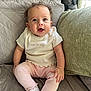 Annie is registered to the contest to win money with this photo: baby, child, smiling, curly_hair, white_top, pink_pants, socks, couch, quilted, green_cushion, indoor, natural_light, happy, sitting, portrait, person, cute, infant, cozy, home
