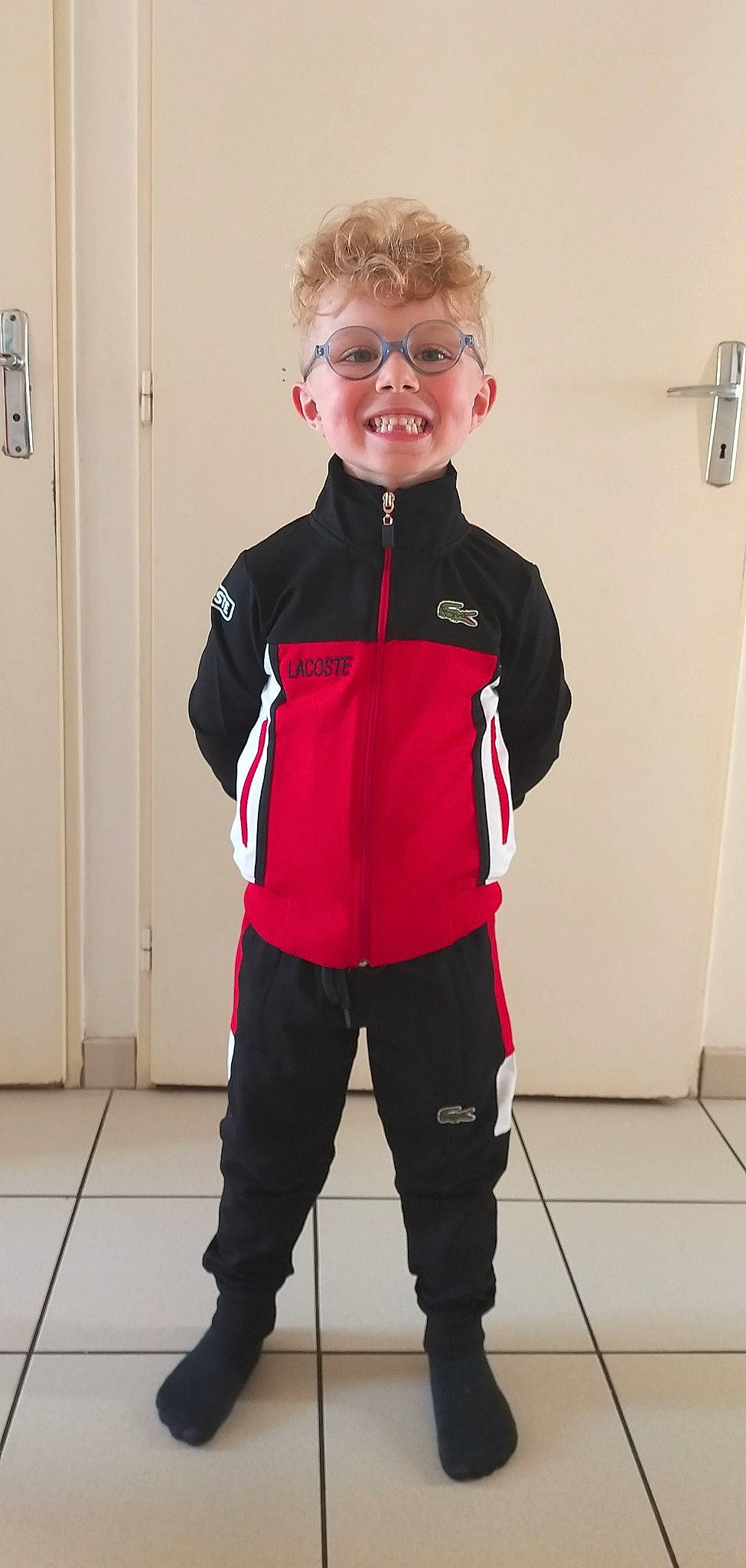 Loys participe au concours pour gagner de l'argent avec cette photo : baby_toddler_clothing, carmine, clothing, cool, door, electric_blue, eyewear, fashion_design, flooring, happy, joy, knee, leg, person, personal_protective_equipment, red, sleeve, smile, sportswear, standing