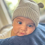 Silas is registered to the contest to win money with this photo: baby, infant, hat, knitted_hat, bear_ears, blue_blanket, close_up, face, eyes, nose, mouth, soft_texture, cozy, resting, indoors, child, portrait, cute, warm, blurred_background