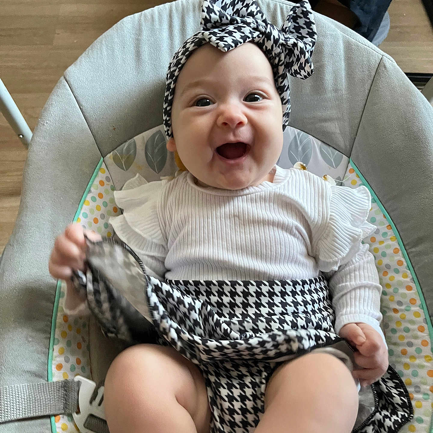Charlotte participe au concours pour gagner de l'argent avec cette photo : apparel, baby, baby_seat, black_and_white, child, clothing, cute, happy, headband, indoors, infant, joyful, legs, patterned_fabric, person, playful, portrait, sitting, smiling, wooden_floor
